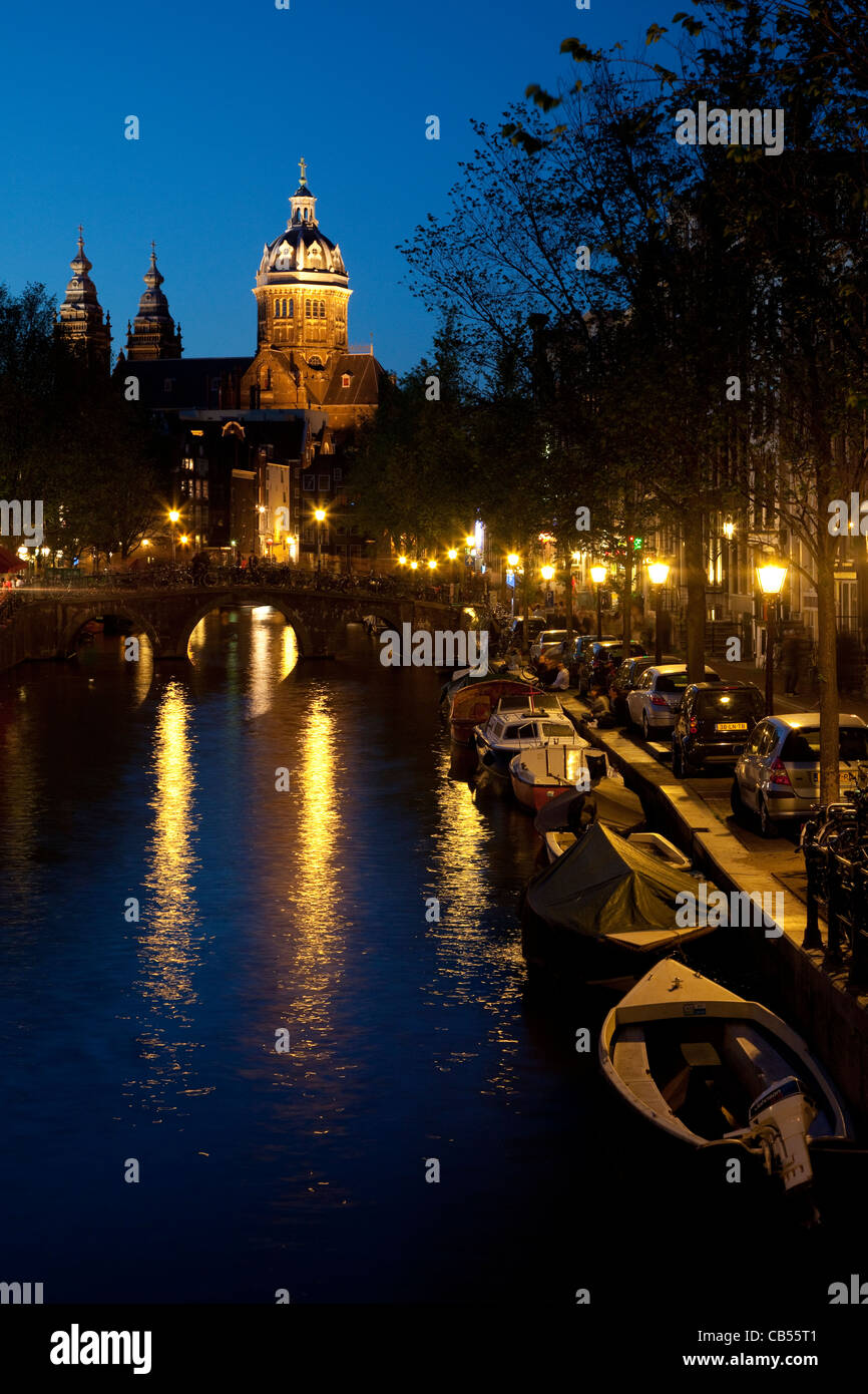 Vista notturna di un canale nel quartiere a luci rosse con Sint-Nicolaaskerk in background. Amsterdam, Paesi Bassi. Foto Stock