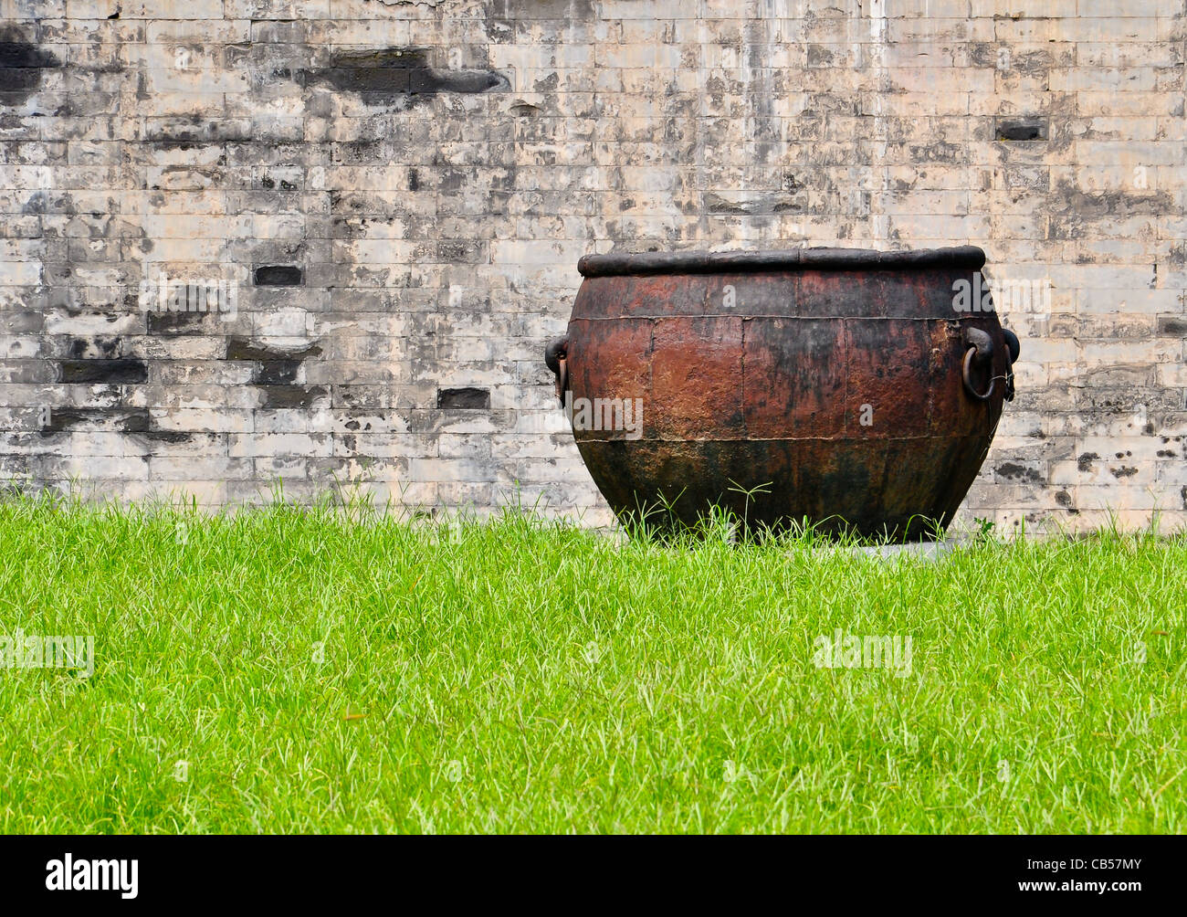 Di ferro arrugginito calderone in un lussureggiante prato di fronte un muro di mattoni Foto Stock