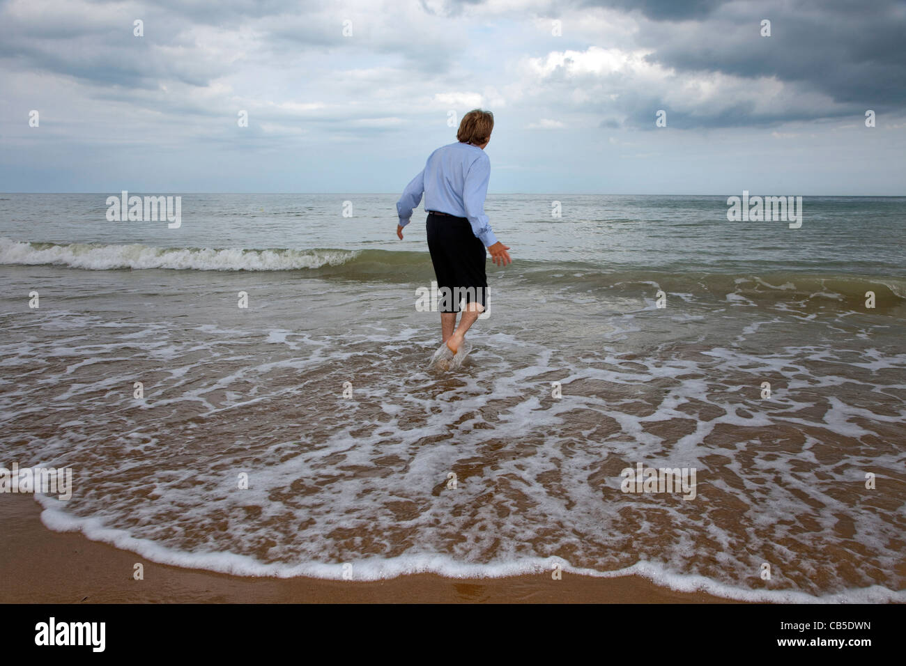 Uomo che indossa arrotolato tuta pantaloni a piedi in mare. Foto Stock