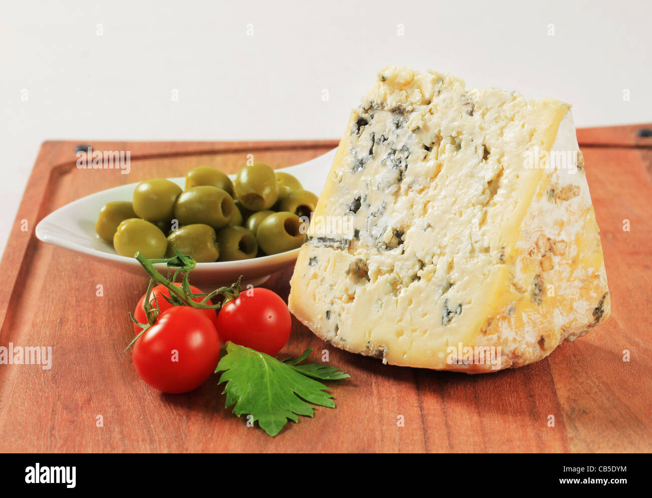 Cuneo di formaggio blu e una ciotola di olive sul bordo di taglio Foto Stock