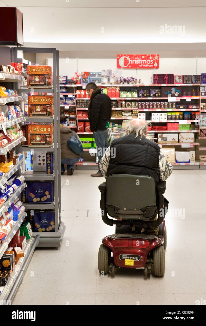 Uomo disabile che acquista sul suo scooter per disabili in un supermercato Waitrose, Regno Unito; accesso disabili negozio Regno Unito. Foto Stock