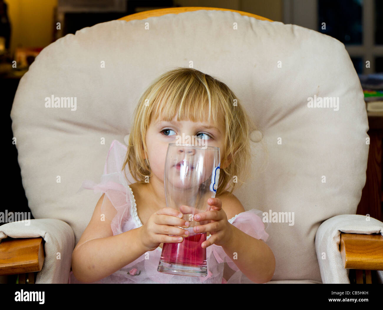 Bambina seduto in una grande sedia, bevendo una rosa (ribes nero) da bere una pinta di vetro Foto Stock