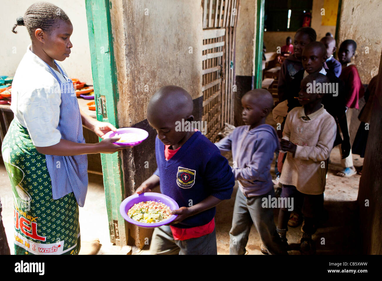 A scuola i bambini ricevono cibo appena cucinato alla scuola di Kibera a Nairobi, dove una ONG corre un pranzo, un programma di alimentazione. Foto Stock