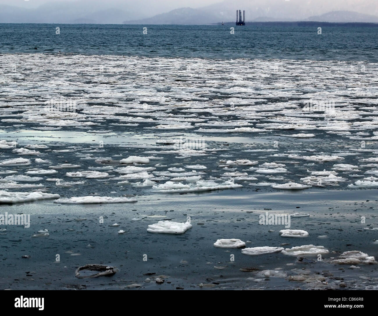 Grandi pezzi di ghiaccio galleggiante in acqua blu di un Alaskan Bay con un jack-up olio impianto di perforazione in background. Foto Stock