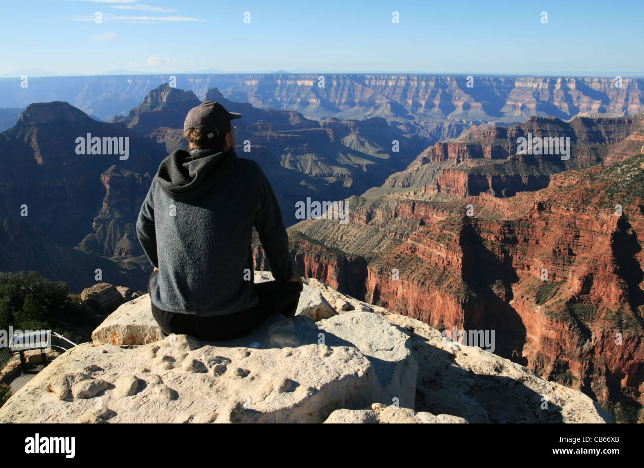 Un uomo seduto su una sporgenza a Bright Angel point guarda oltre il bordo settentrionale del Grand Canyon, Arizona Foto Stock