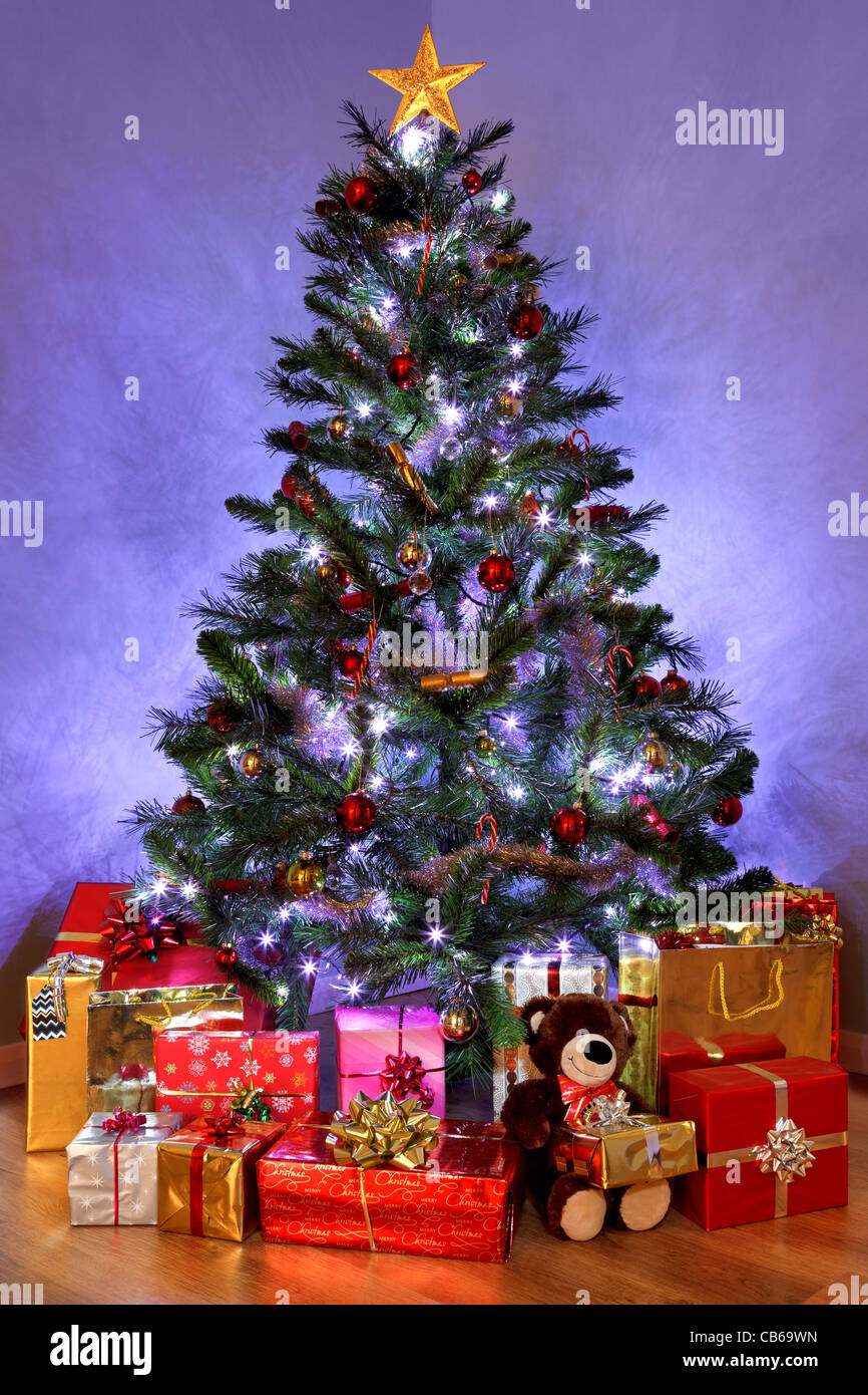 Foto di un albero di Natale con le decorazioni e le luci fairy circondato da presenta su di un pavimento in legno Foto Stock