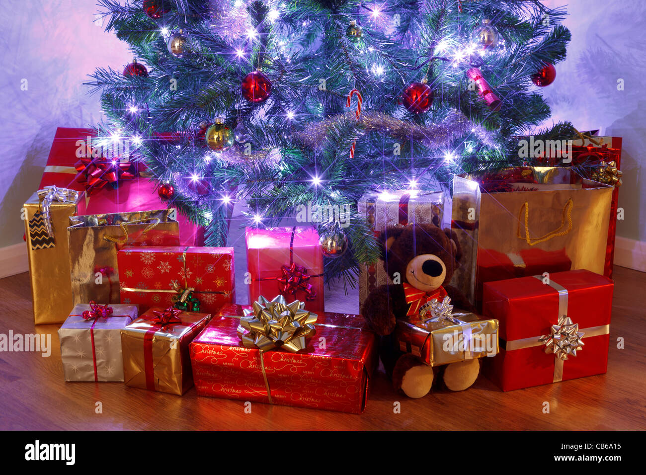Foto di un albero di Natale con le decorazioni e le luci fairy circondato da presenta su di un pavimento in legno Foto Stock
