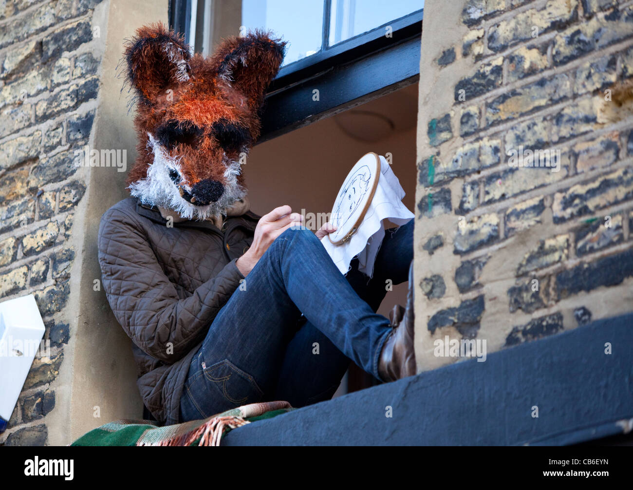 Uomo seduto su un davanzale indossando un fox maschera di testa e cucire a mano con un cerchio, Columbia Road Market, London, England, Regno Unito Foto Stock