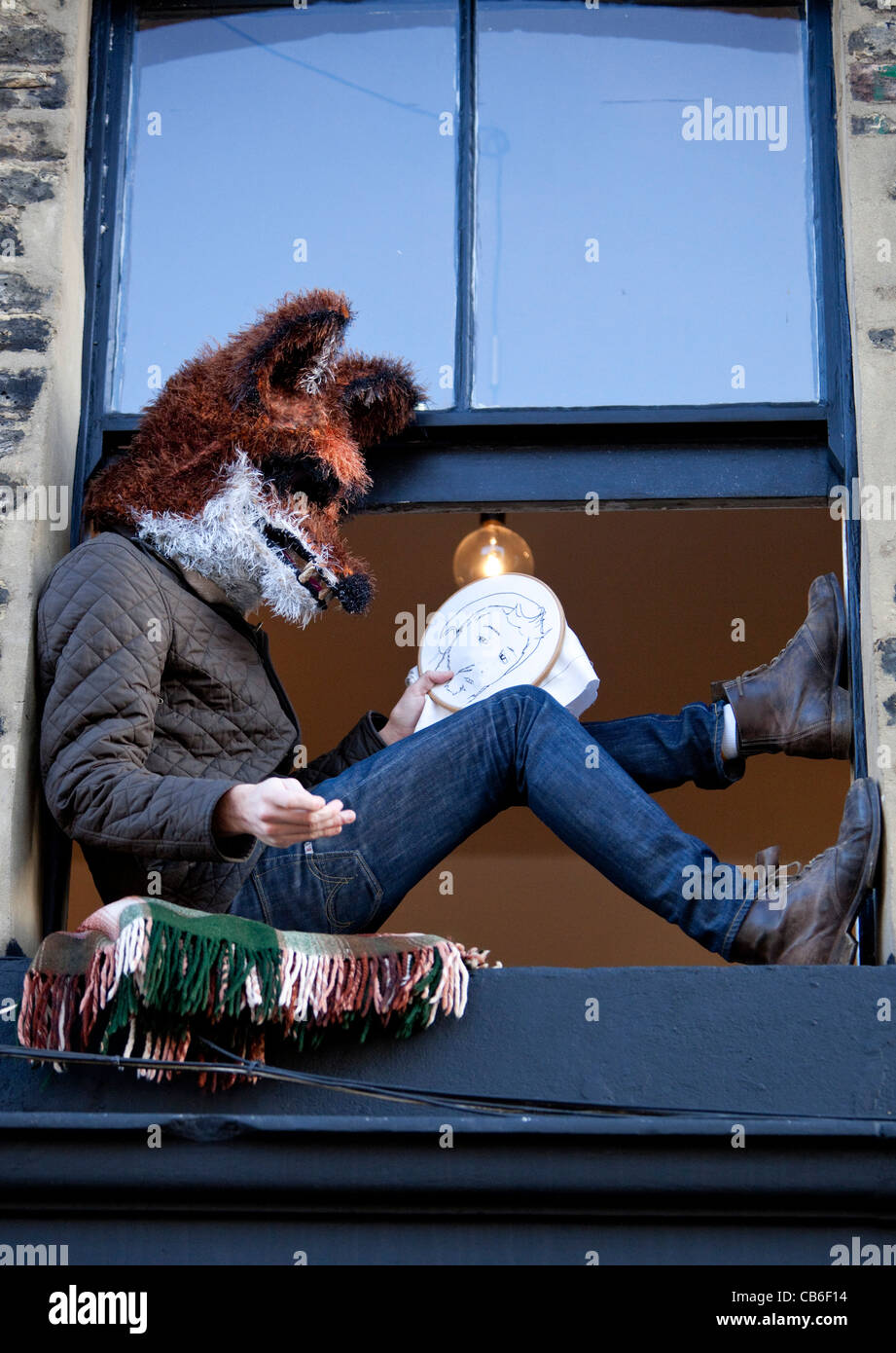 Uomo seduto su un davanzale indossando un fox maschera di testa e cucire a mano utilizzando un cerchio da ricamo di Londra, Inghilterra, Regno Unito, GB Foto Stock