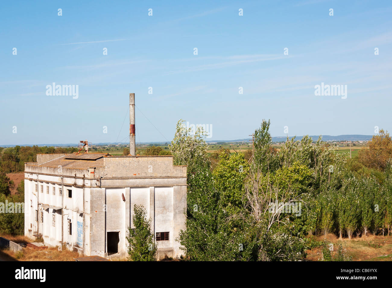 Vecchia fabbrica abbandonata contro la foresta e il cielo blu Foto Stock