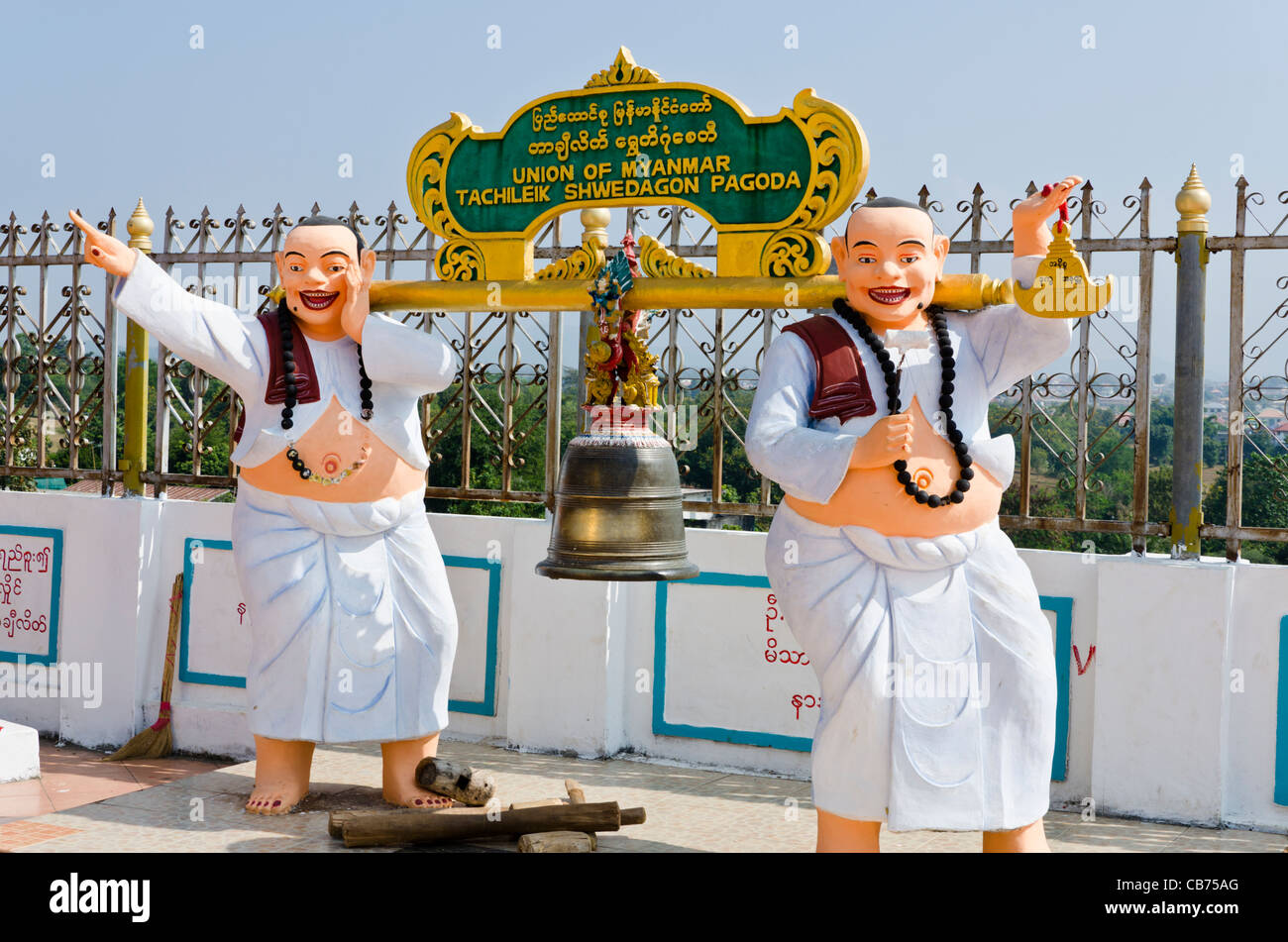 Statue di 2 fat sorridente uomini in abiti bianchi tenendo un polo di oro fino con una campana a Tachiliek Shwe Dagon Pagoda in Myanmar Foto Stock