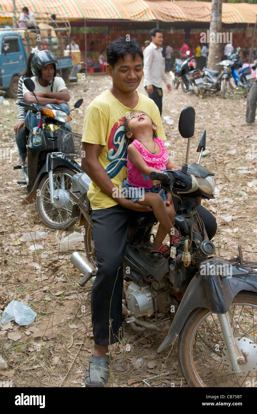 Sorridente cambogiano con sua figlia seduta su un ciclomotore in un villaggio di festa, Cambogiano nuovo anno (Chaul Chnam Thmey), Bakong Village, Siem Reap, Cambogia Foto Stock