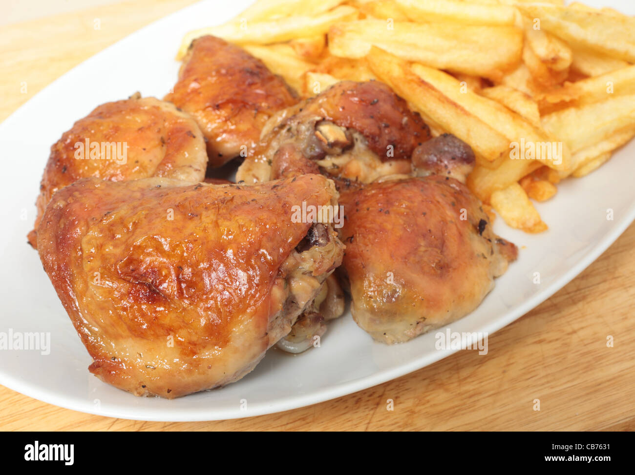 Un piatto impilati con limone arrosto cosce di pollo e patatine fritte, o chip, con un cucchiaio Foto Stock