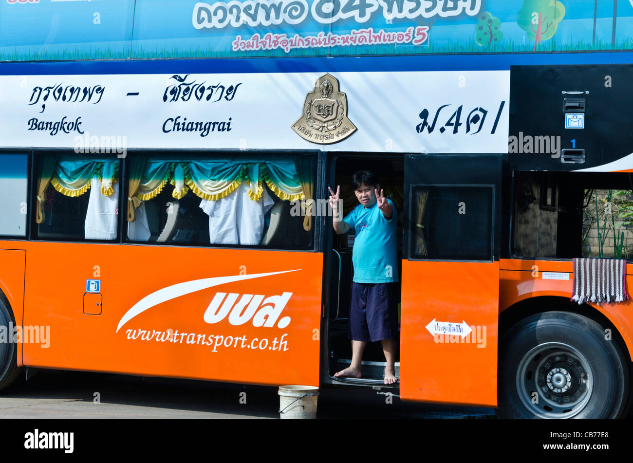 Uomo di pulizia bus di lusso sorge nel portale in sole e rende V segni a Maesai Bus Terminal in Thailandia del Nord Foto Stock