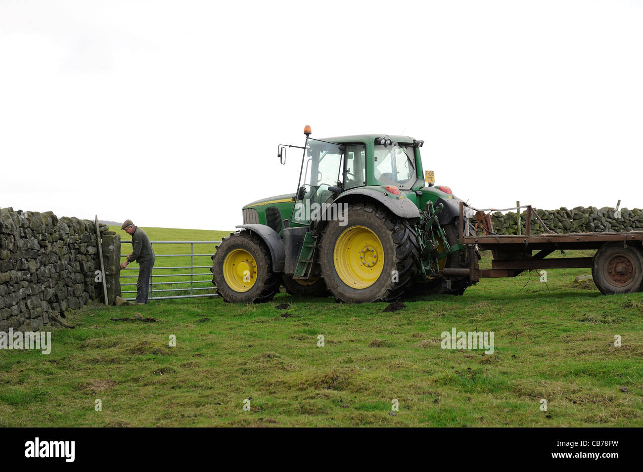 Un agricoltore l'apertura di un cancello in un campo con il suo trattore e rimorchio England Regno Unito Foto Stock