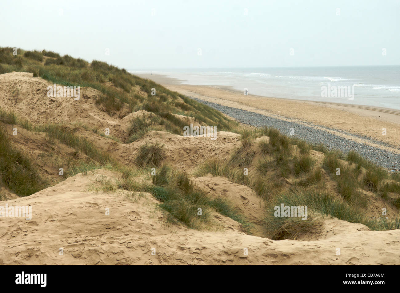 La figura camminando lungo la spiaggia tra il mare e le dune di sabbia Foto Stock