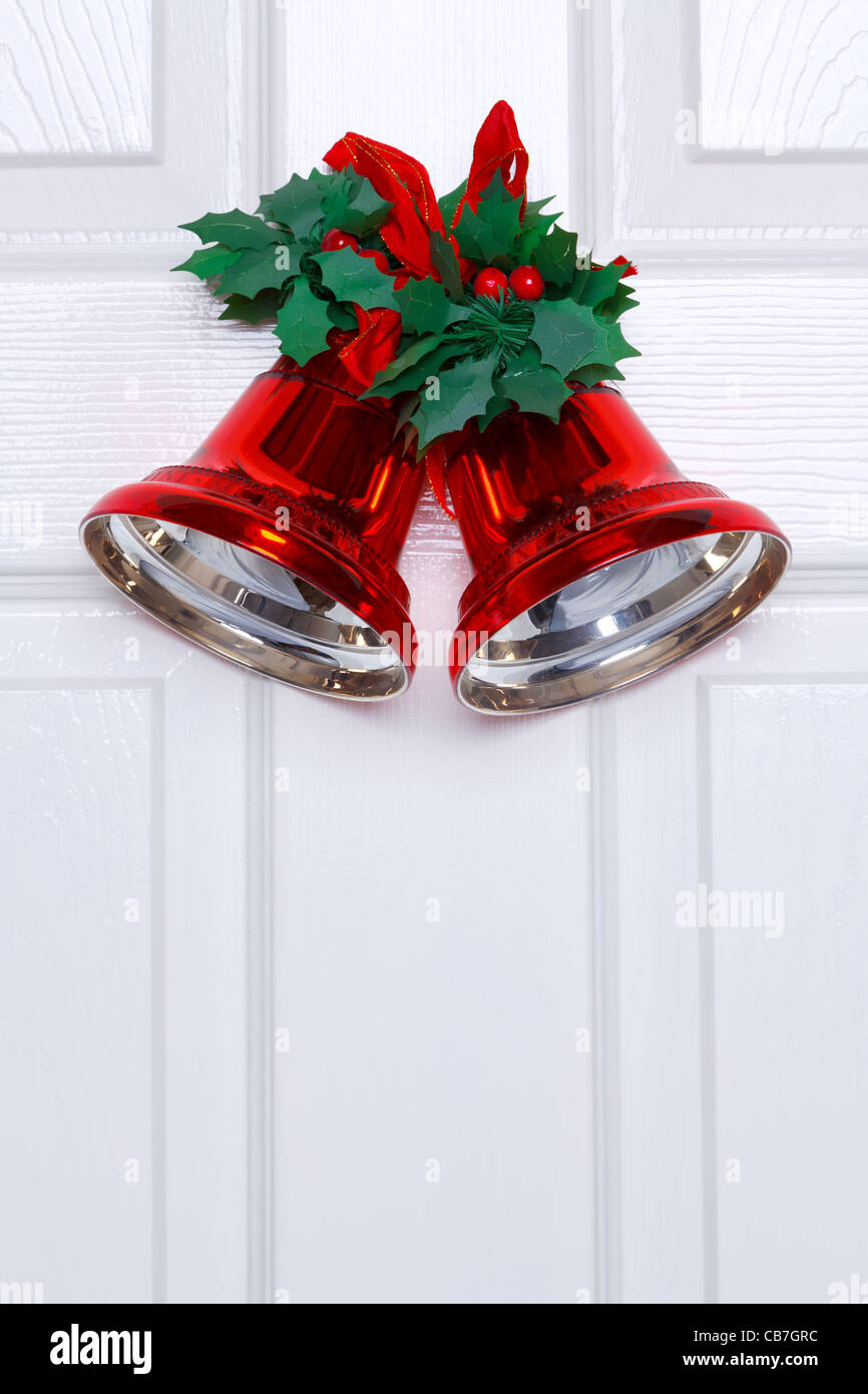 Foto di rosso le campane di Natale con finti holly e nastro appeso su una porta bianca. Foto Stock