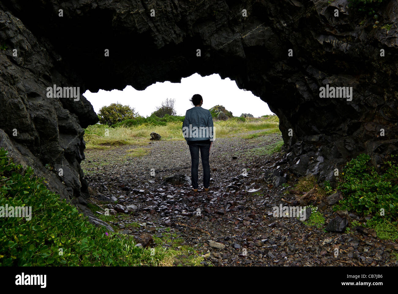 Giovane donna in piedi fuori pioggia nel rifugio di roccia naturale arch Moa punto Wellington Nuova Zelanda Foto Stock