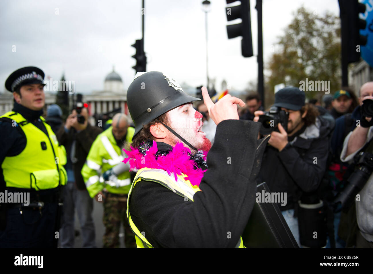 Un dimostratore maschio indossa clown make up e polizia in plastica casco in Trafalgar Square a Londra. Foto Stock