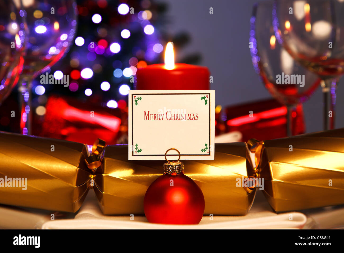 Foto di una cena di Natale posto impostazione e ninnolo il titolare della carta con decorate albero fuori fuoco in background. Foto Stock