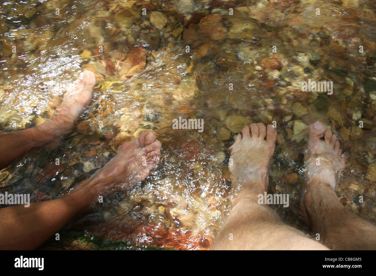 Un uomo e una donna ammollo due coppie di piedi stanchi in un flusso dal ginocchio in giù Foto Stock