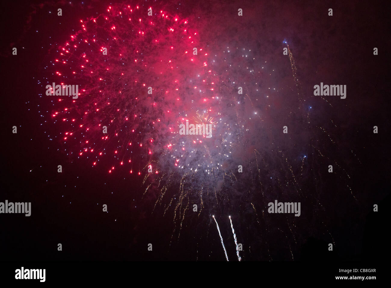 Enorme rosso fuoco d'artificio esplosione con piccole esplosioni in background. Striature di luce e nuvole di esplosione. Foto Stock