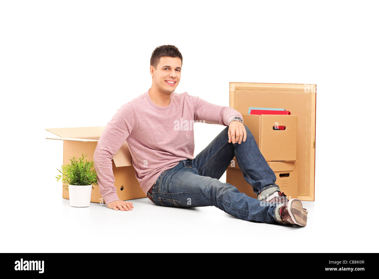 Uomo sorridente in appoggio da traslocare in una nuova casa con scatole intorno a lui Foto Stock