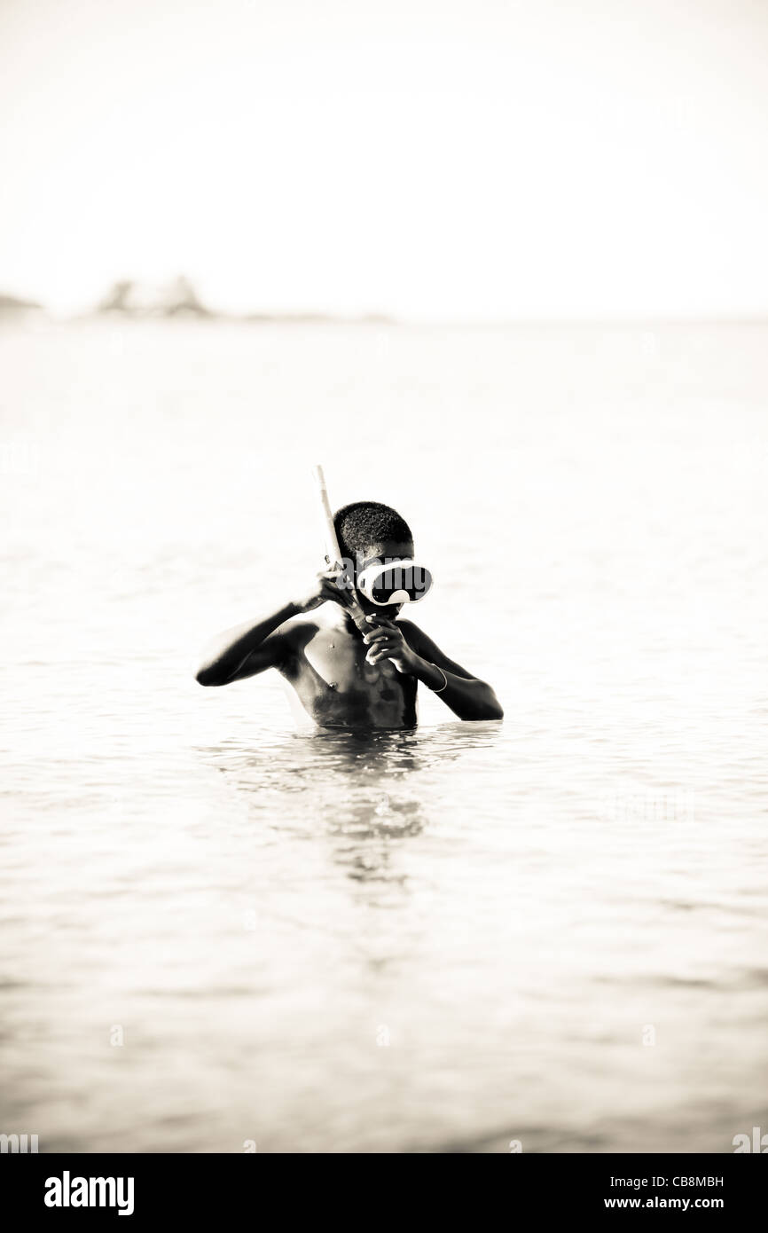 Un mezzo sommerso giovane ragazzo con equipaggiamento da snorkelling regola il suo fare snorkeling a Ampangorinana, Nosy Komba, a nord-ovest del Madagascar, Africa Foto Stock