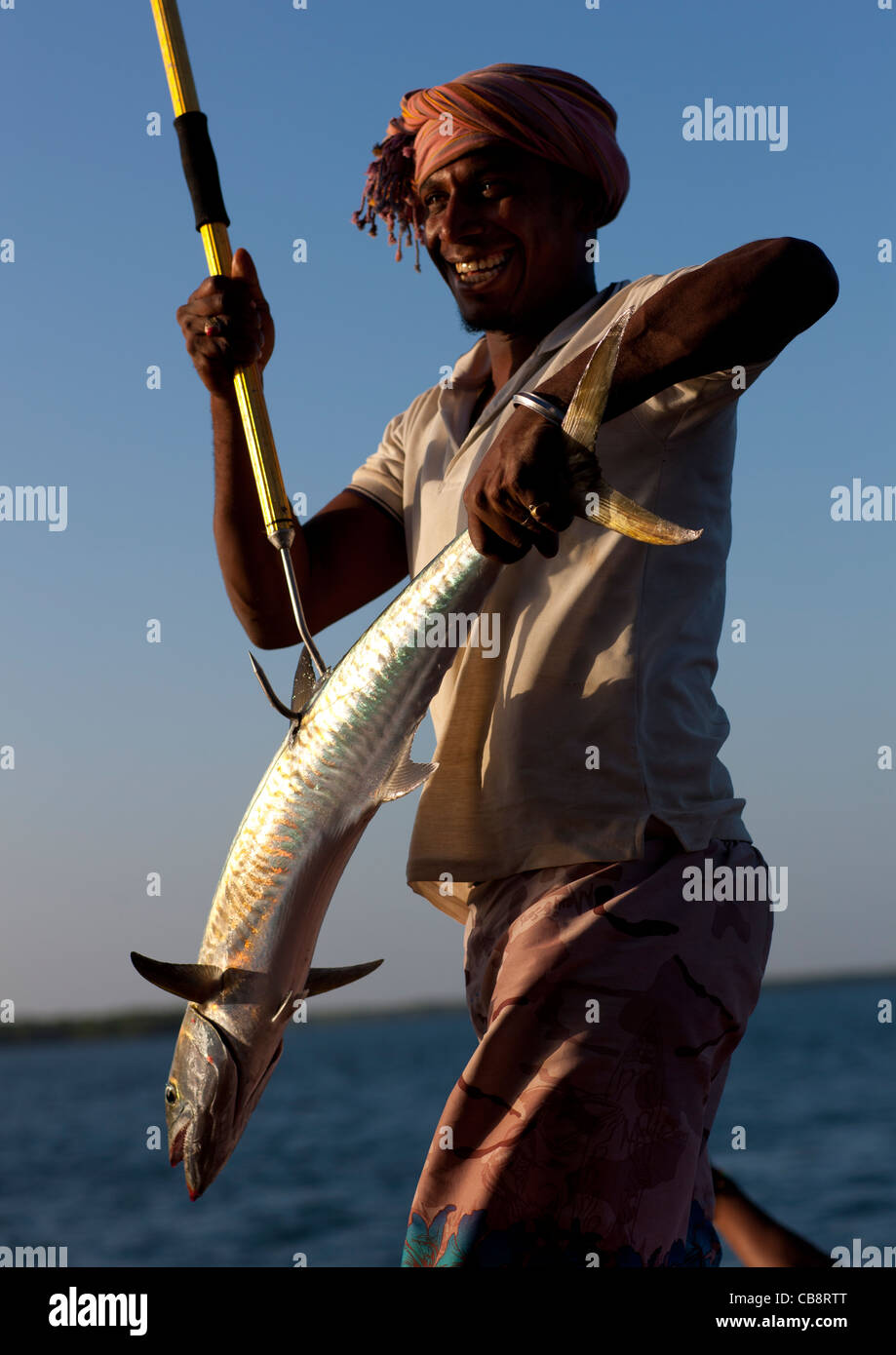 Uomo Turbanned Holding argenteo sorridendo pesce agganciato Stick, Lamu, Kenya Foto Stock