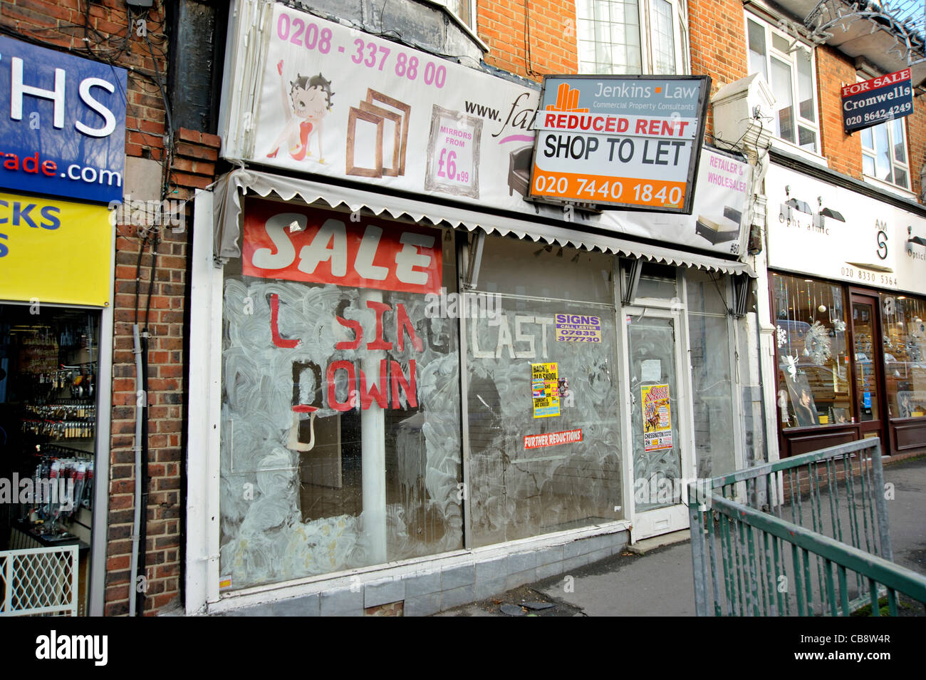 Un negozio di vuoto in un suburbano di Londra high street con 'chiusura di vendita " sulla sua finestra e una scheda Agenti offrendo canone ridotto. Foto Stock