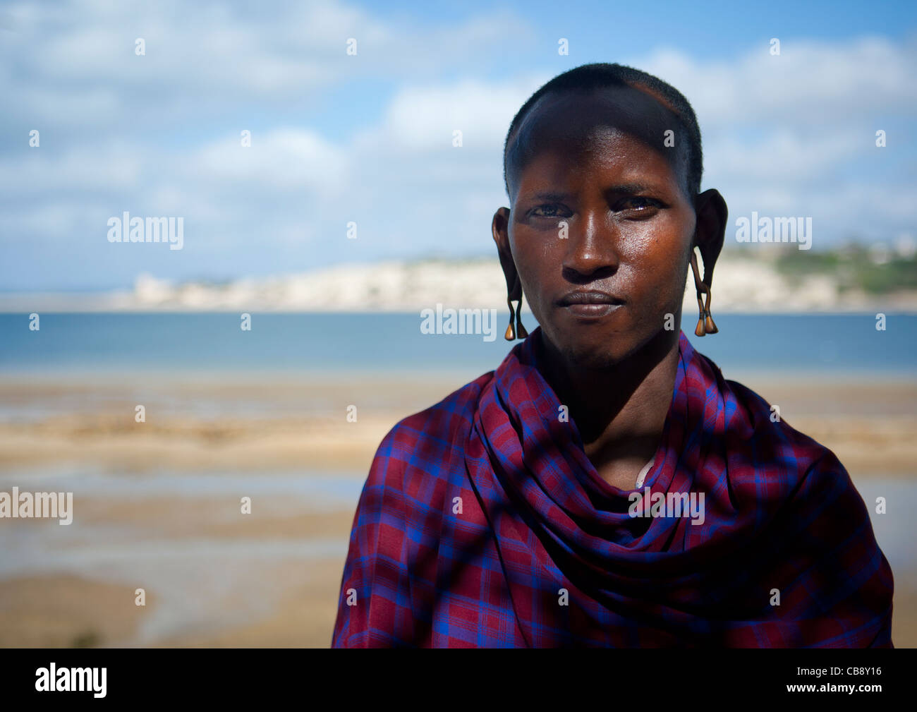 Uomo Masai Keeper con la testa rasata e abiti tradizionali con il mare in background, Lamu, Kenya Foto Stock