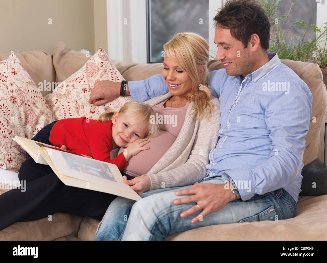 La famiglia felice la visione di album di foto. Donna incinta, papà e la loro figlia aspetta un altro bambino. Foto Stock