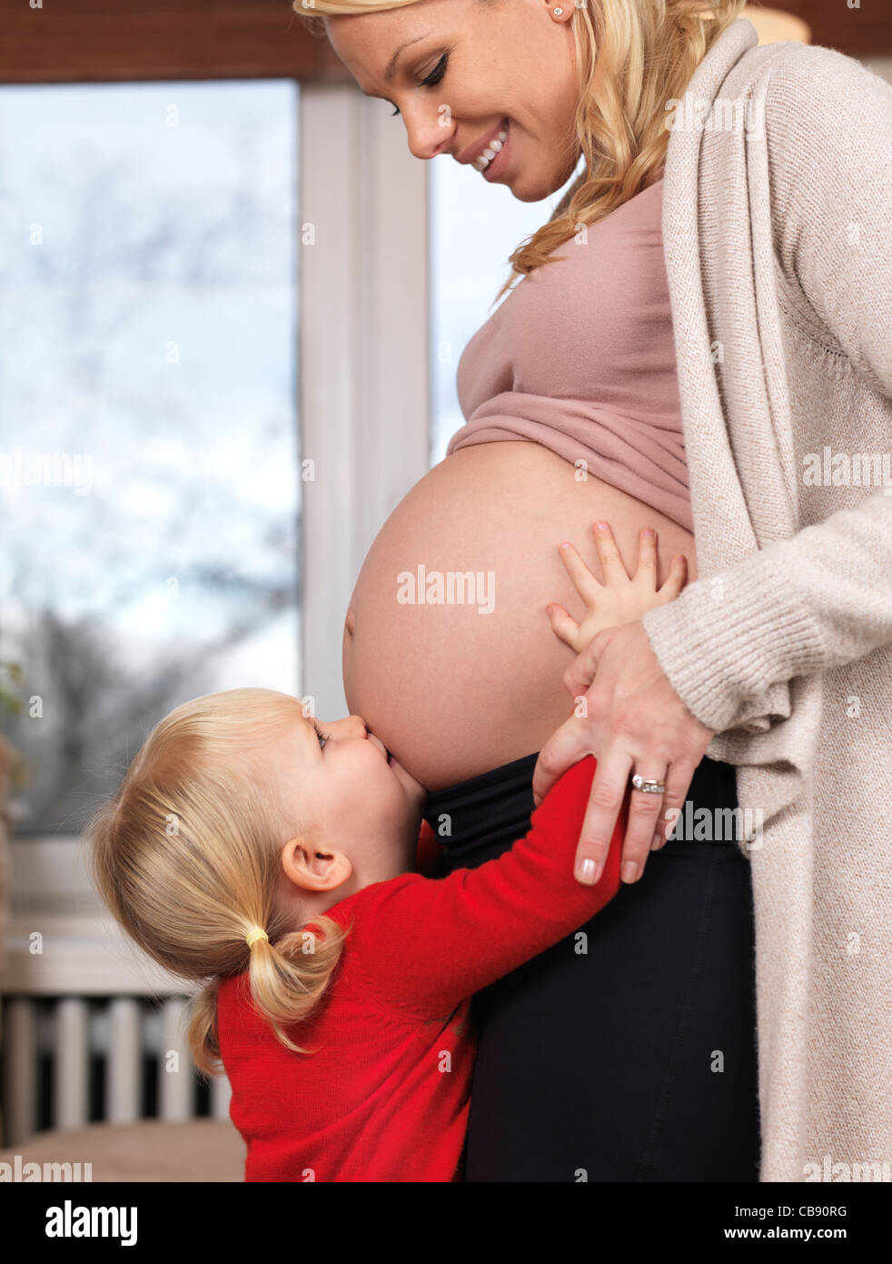 Piccola figlia bacia felice in stato di gravidanza della madre ventre Foto Stock