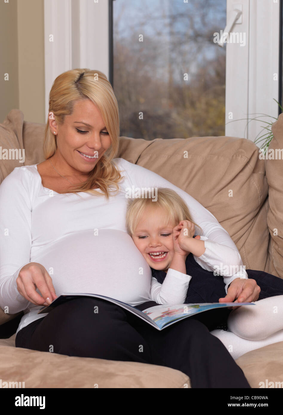 Felice di gravidanza madre e la sua figlia di tre anni la lettura di un libro insieme a casa Foto Stock