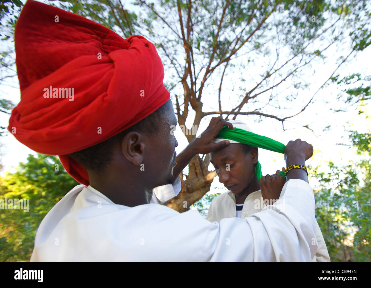 Rosso uomo Turbanned Putting Green turban sul un altro ragazzo in testa, Maulidi, Lamu, Kenya Foto Stock