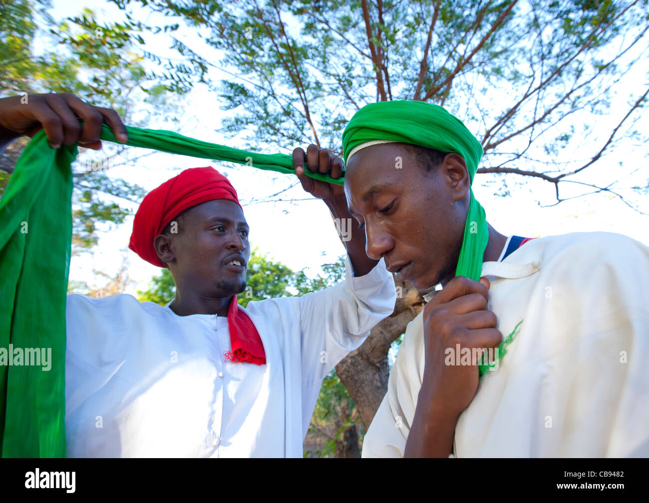 Rosso uomo Turbanned Putting Green turban sul un altro ragazzo in testa, Maulidi, Lamu, Kenya Foto Stock