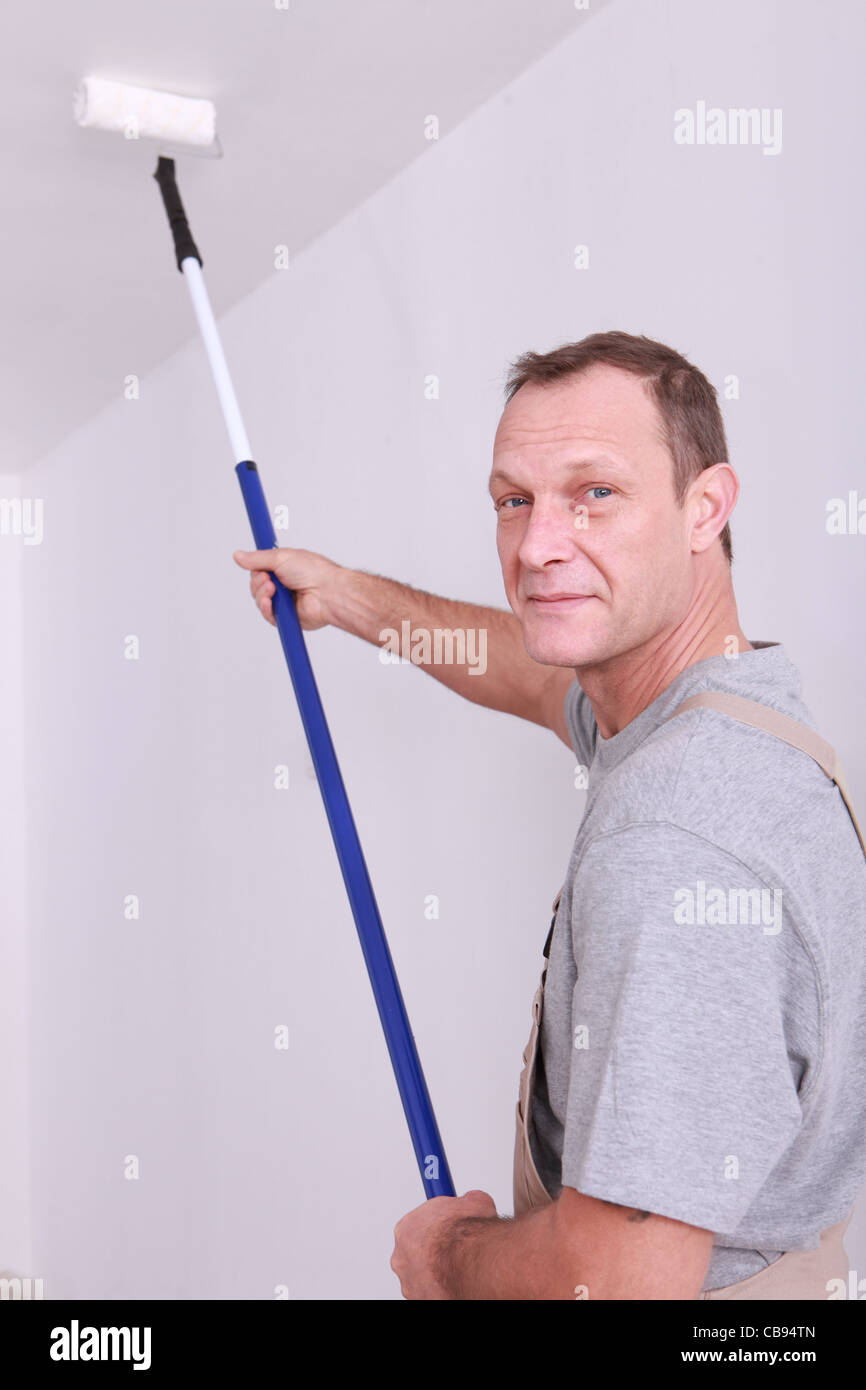 Arredatore usando un rullo lungo a dipingere un soffitto Foto Stock