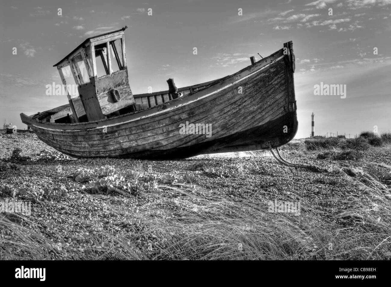 Un vecchio abbandonato la pesca in barca sulla spiaggia di Dungeness, Kent, Regno Unito. La Dungeness faro è in background. Foto Stock