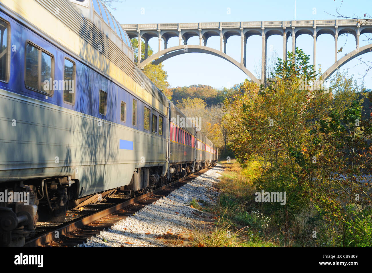 Un treno passeggeri sotto un alto ponte in una zona panoramica Foto Stock