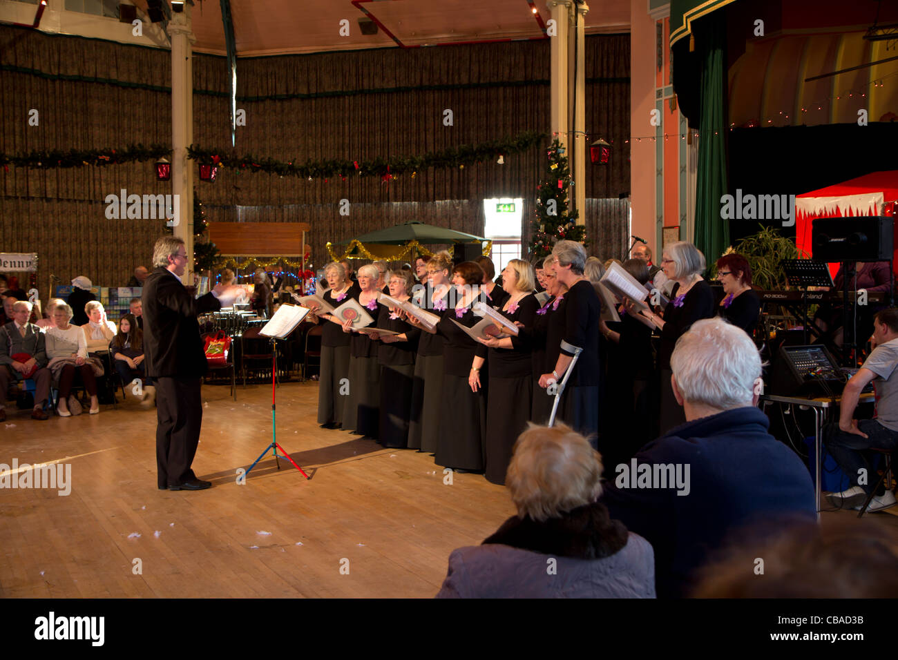Conduttore di musica con coro femminile a Dickensian mercatino di Natale nel Padiglione Hall Buxton Derbyshire Peak District Inghilterra Foto Stock