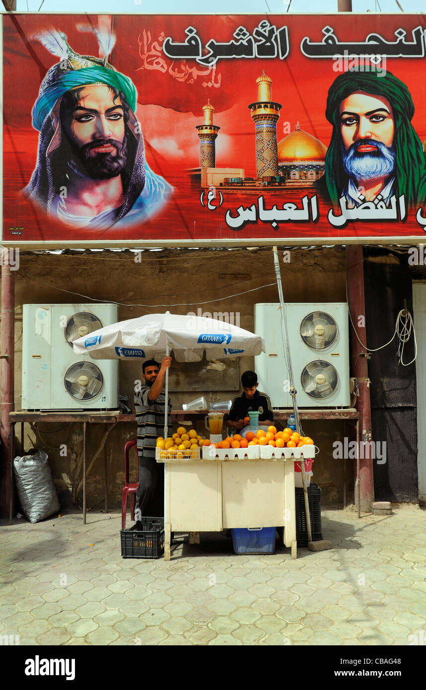 L'Iraq, Najaf, un succo di arancio sostare al di sotto di un grande poster di Imam Ali Foto Stock