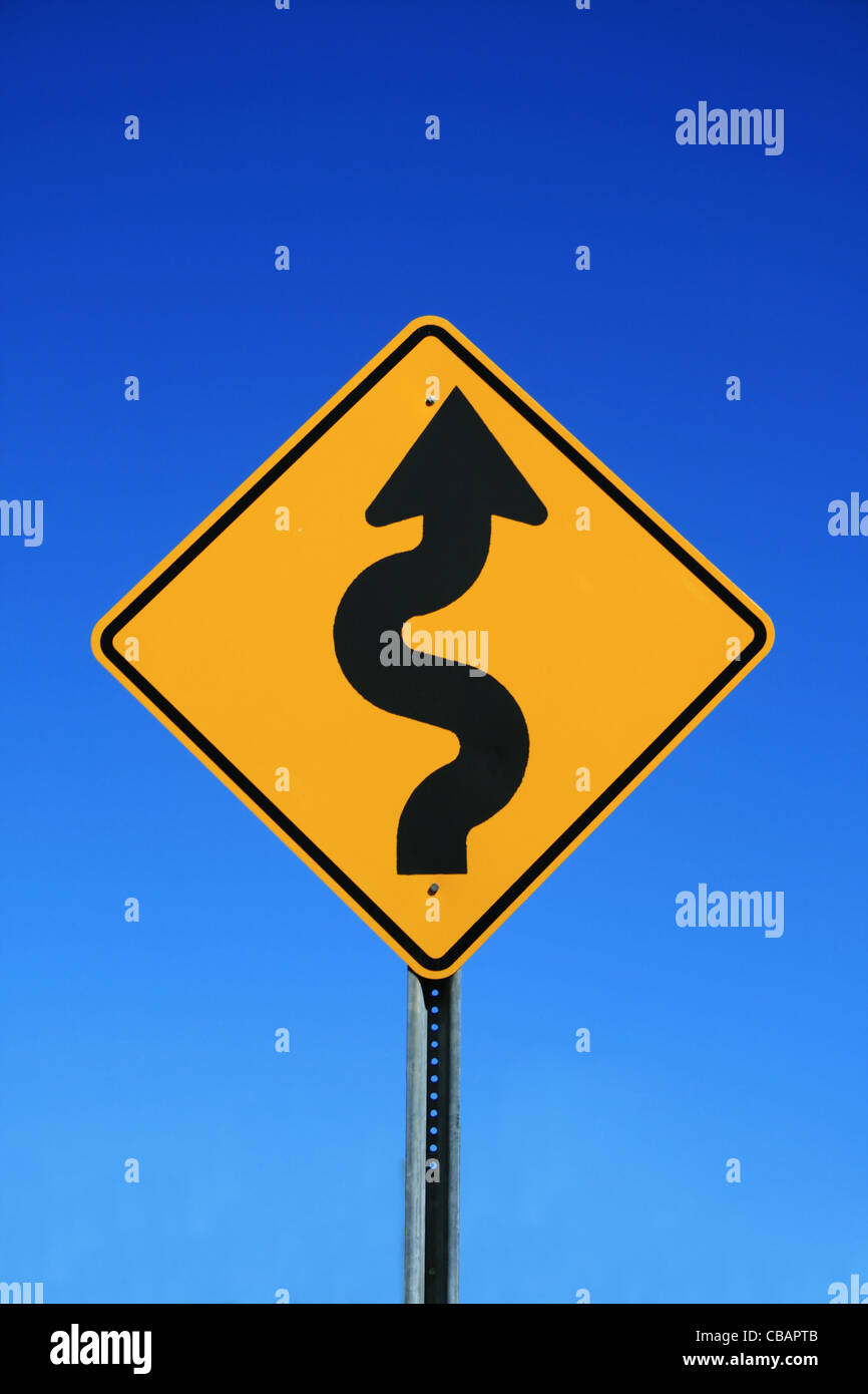 Winding Road Sign in giallo e nero su blu sullo sfondo del cielo Foto Stock