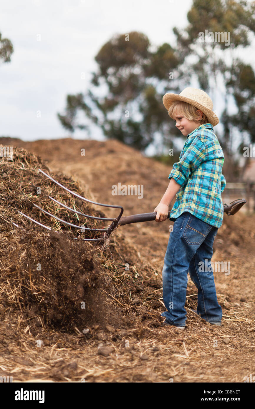 Boy utilizzando forcone nel pagliaio Foto Stock