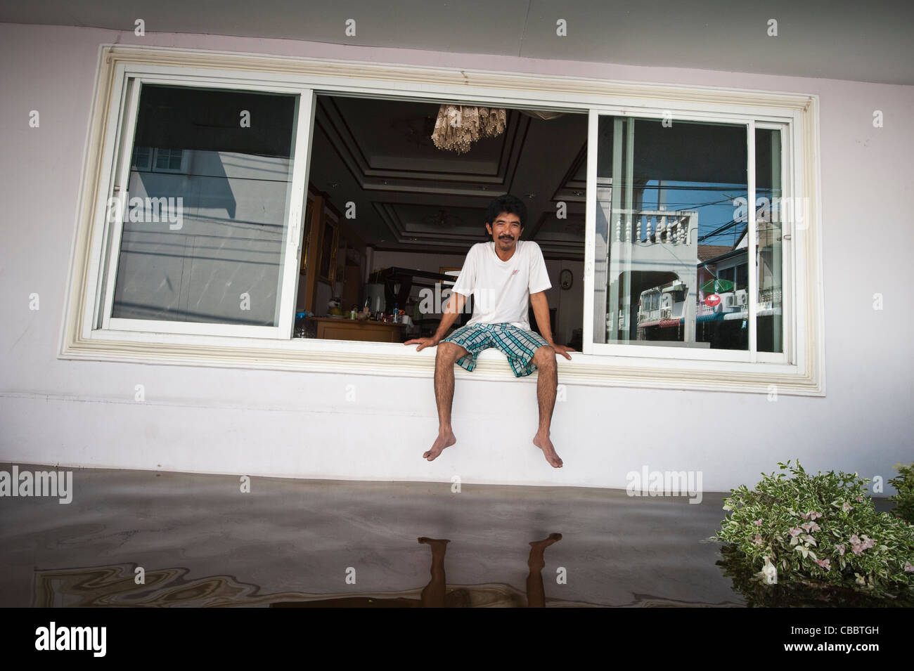 Un uomo seduto in una finestra e guardare come le alluvioni sorge fuori la sua casa nei pressi di Don Muang, Bangkok. Foto Stock