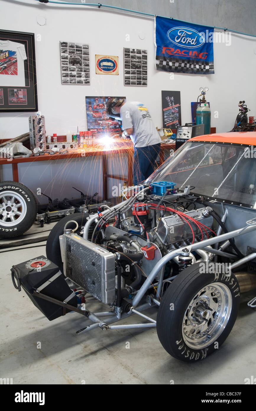 Drag racing ventilatori durante le riparazioni per la sua Ford Mustang e la saldatura nel suo laboratorio Foto Stock