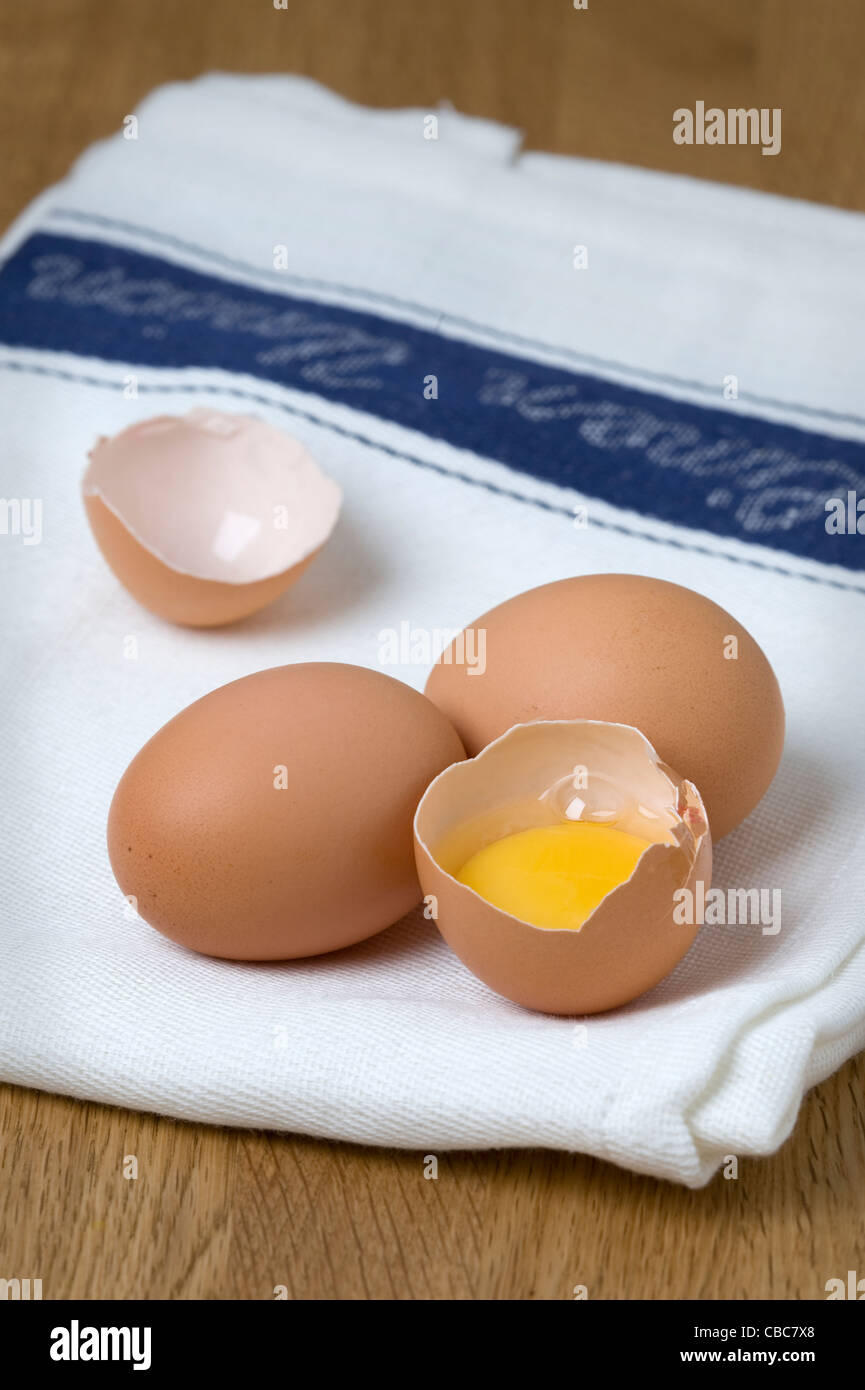 Brown uova di galline su un tè bianco asciugamano con un acciaio inossidabile Sbattere un uovo rotto e separata che mostra il bianco d'uovo e il tuorlo d'uovo Foto Stock