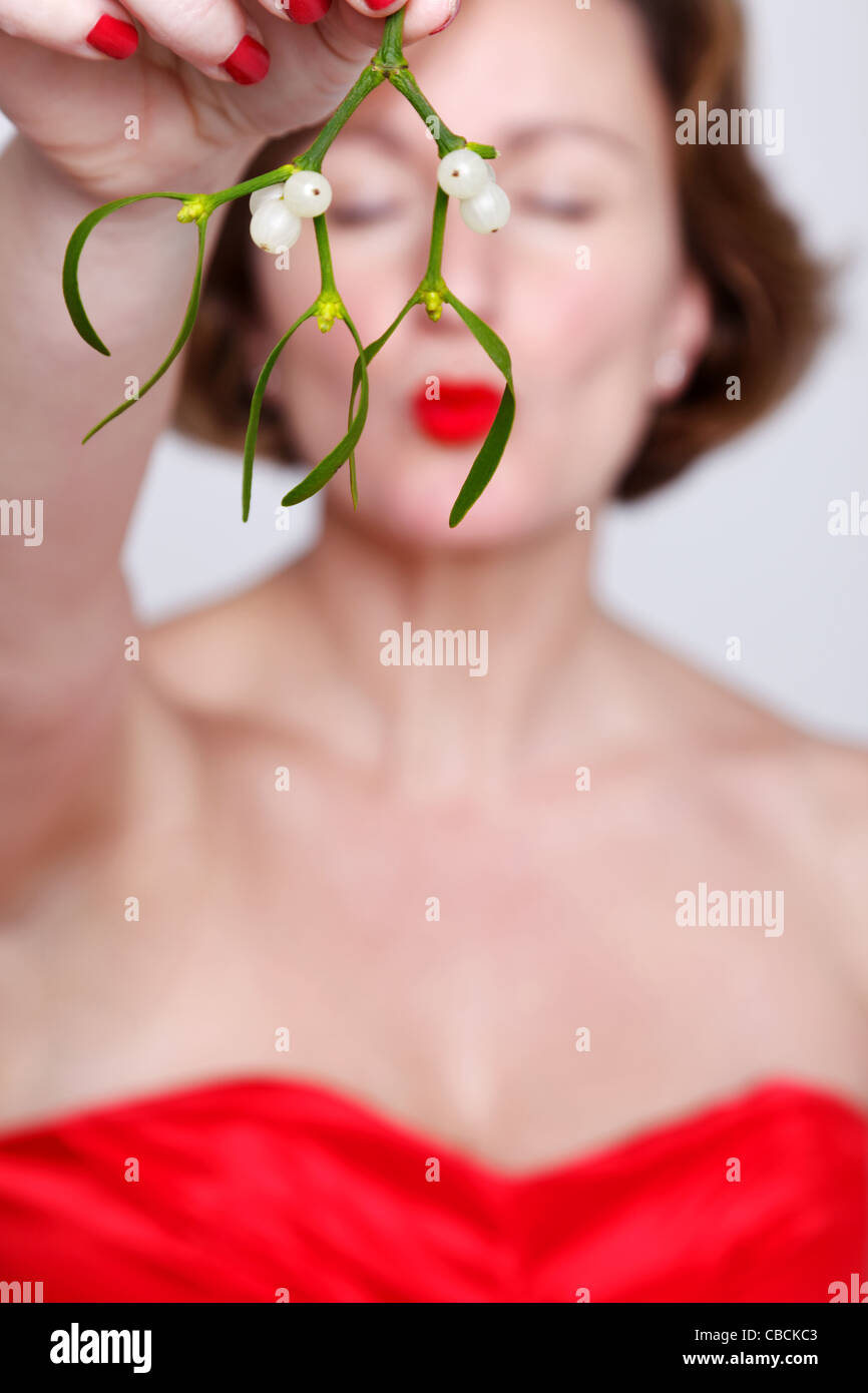 Foto di una ragazza in un abito rosso tenendo alcuni vischio e baciare con gli occhi chiusi. Foto Stock