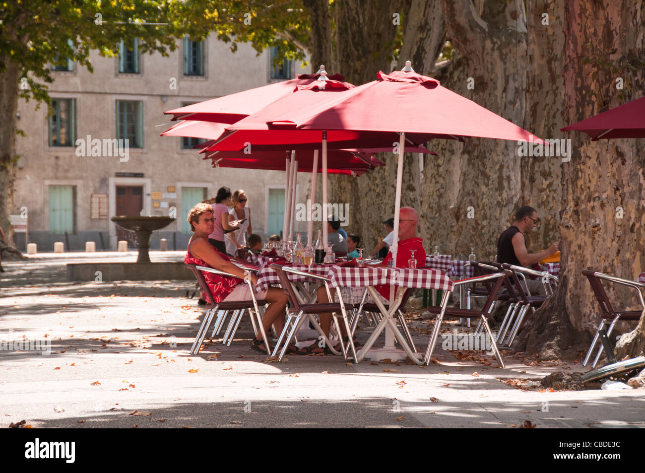 Le persone che si godono le bevande sotto gli ombrelloni in una calda giornata estiva in un cafe' sul marciapiede nel centro della città di Gignac Herault Foto Stock