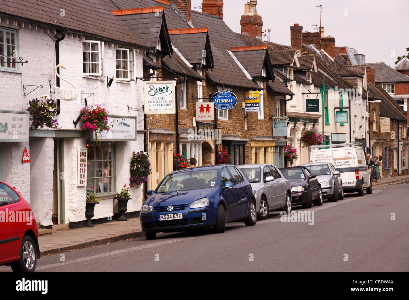 Storico negozio fronti, segni e automobili parcheggiate lungo il centro dello shopping, Mill Street, Oakham, Rutland, England, Regno Unito Foto Stock