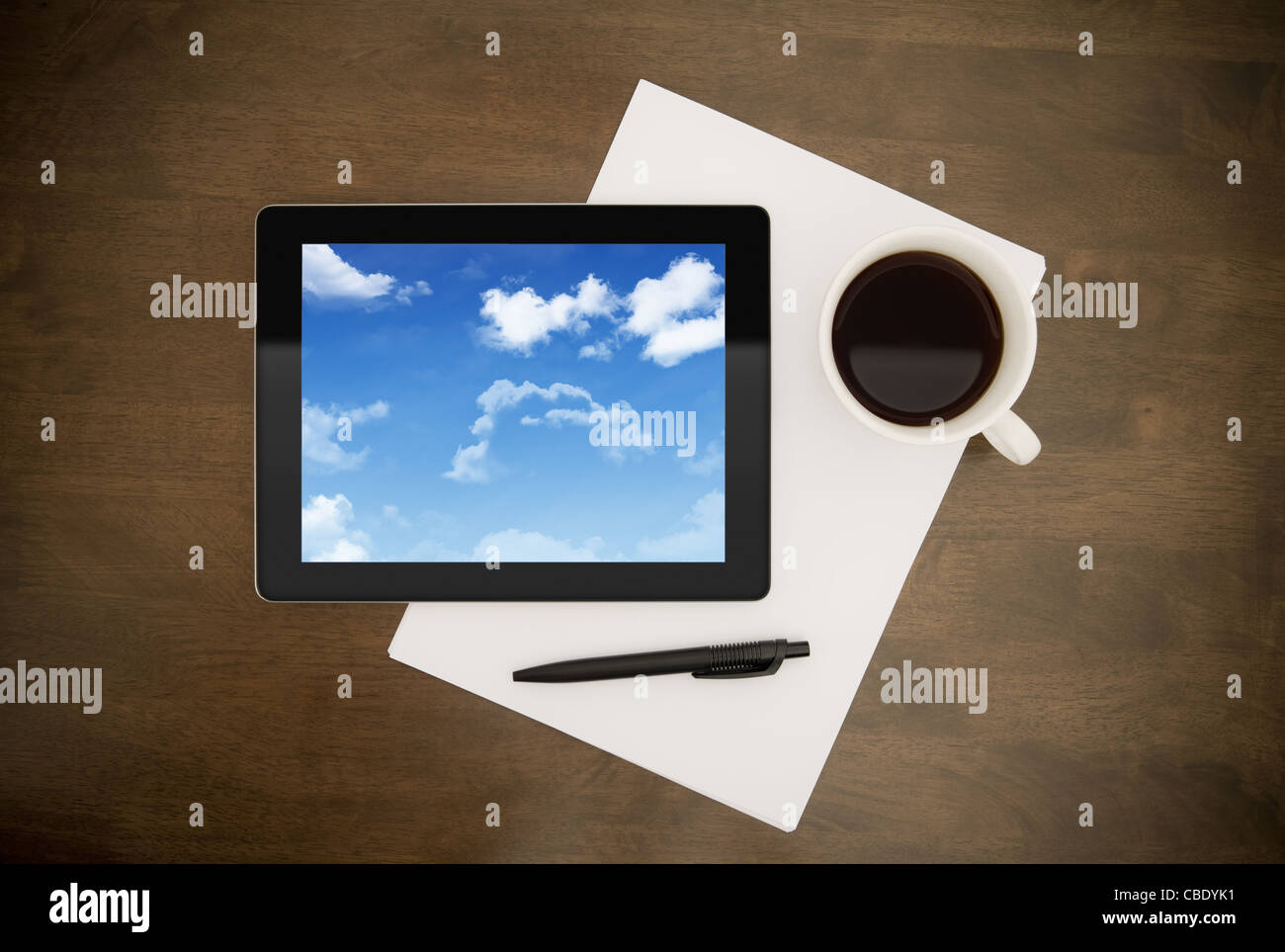 Tavoletta digitale con le nuvole sullo schermo giacente sul piano di lavoro con carta e penna e la tazza di caffè. Concetto di immagine sul cloud computing di loro Foto Stock
